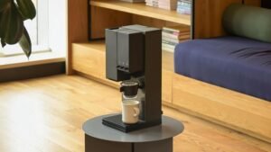 Minimalist xBloom All-in-One coffee machine on a grey circular table in a modern interior, featuring an automated pour-over brewing system for specialty coffee enthusiasts.